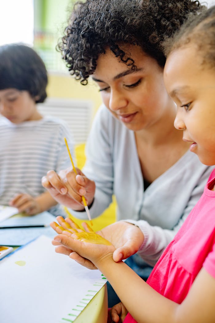 Teacher assists children with painting in a vibrant, creative classroom setting.
